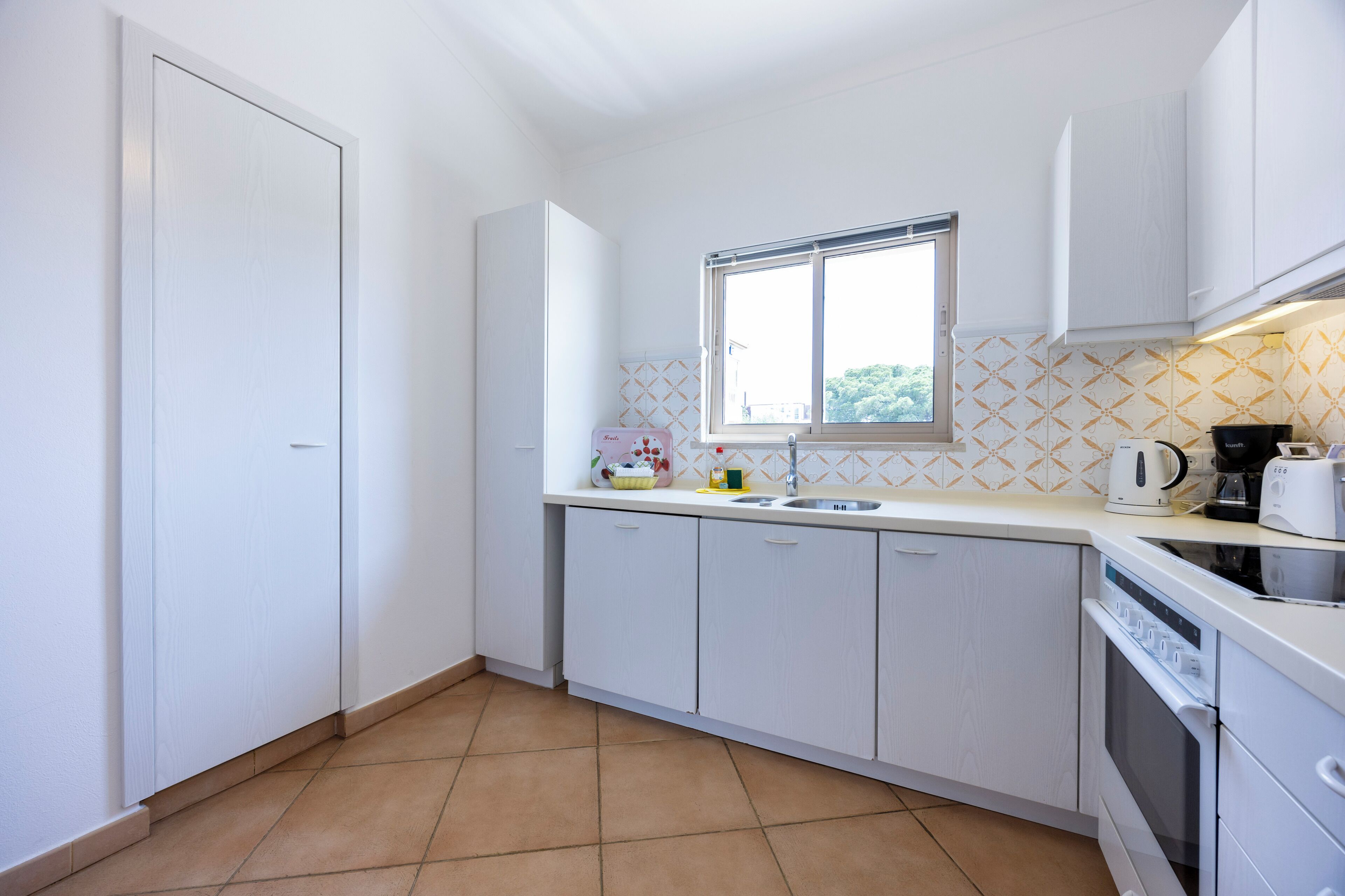 A compact kitchen with white cabinets, a window, and a tiled backsplash.