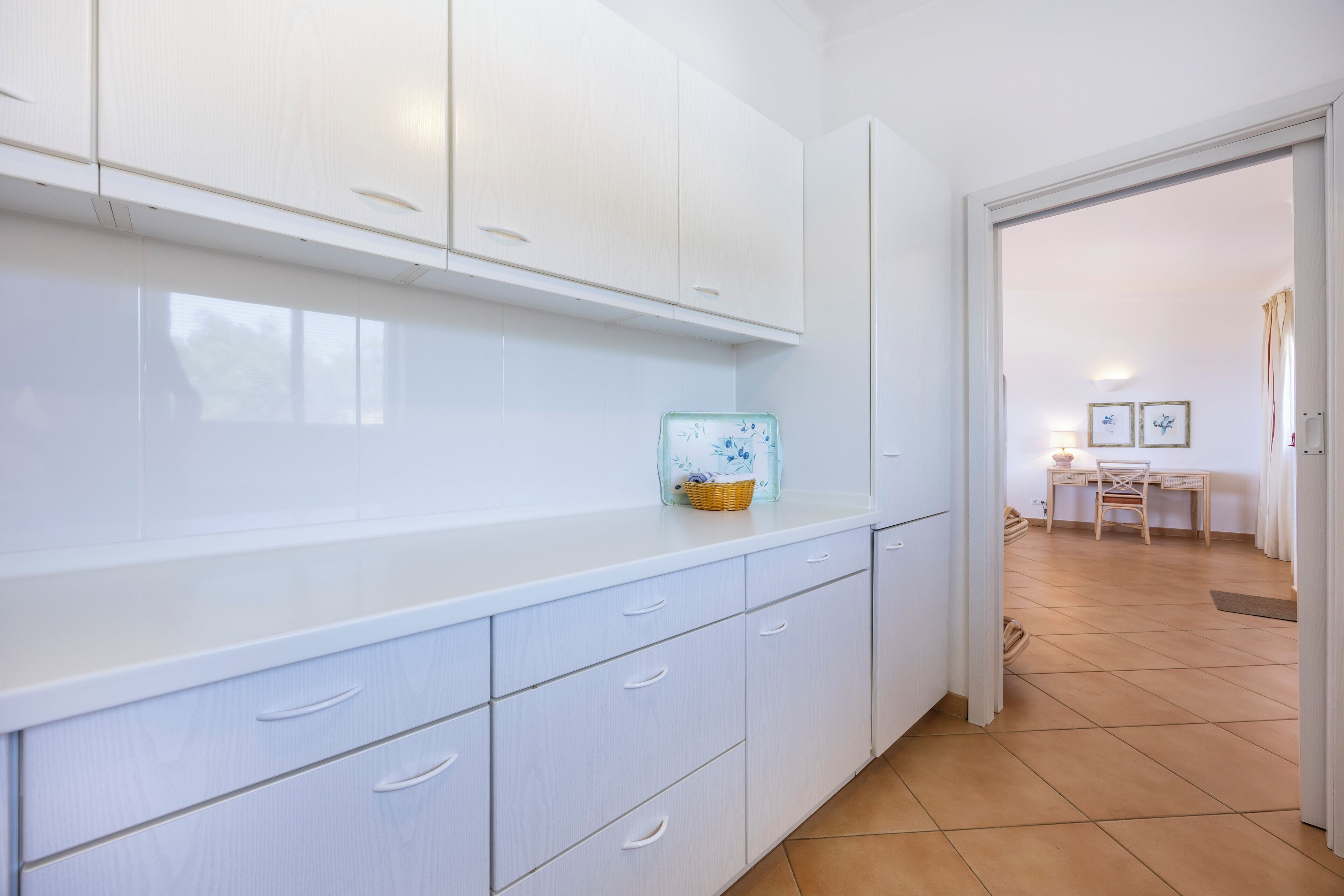 A kitchen with white cabinets, a countertop, and a tiled floor.