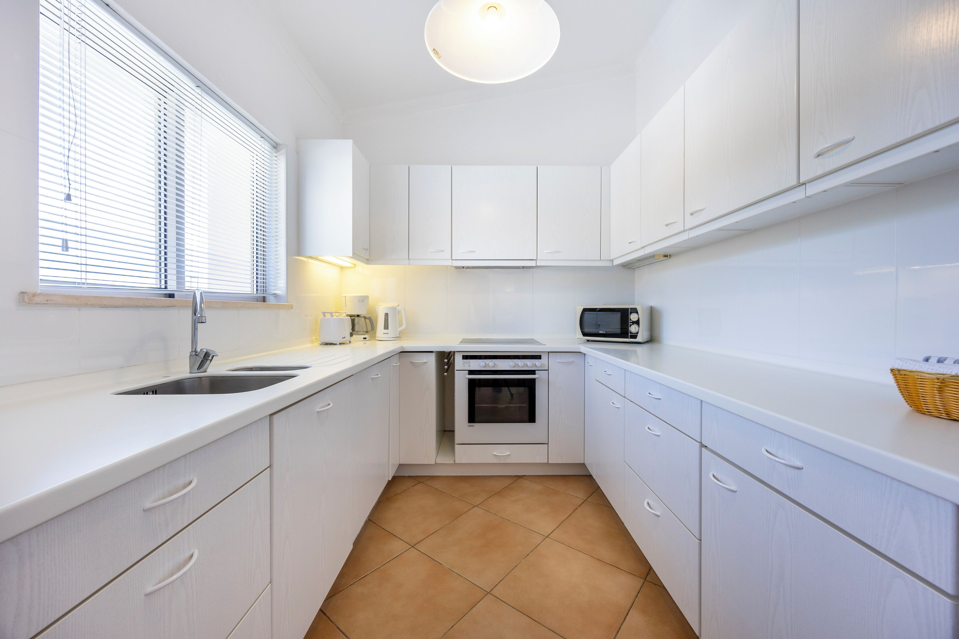 A compact kitchen with white cabinets, a sink, a stove, and a microwave.