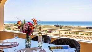 Tavolo apparecchiato per due con una bottiglia di vino e un vaso di fiori, con vista sulla costa.