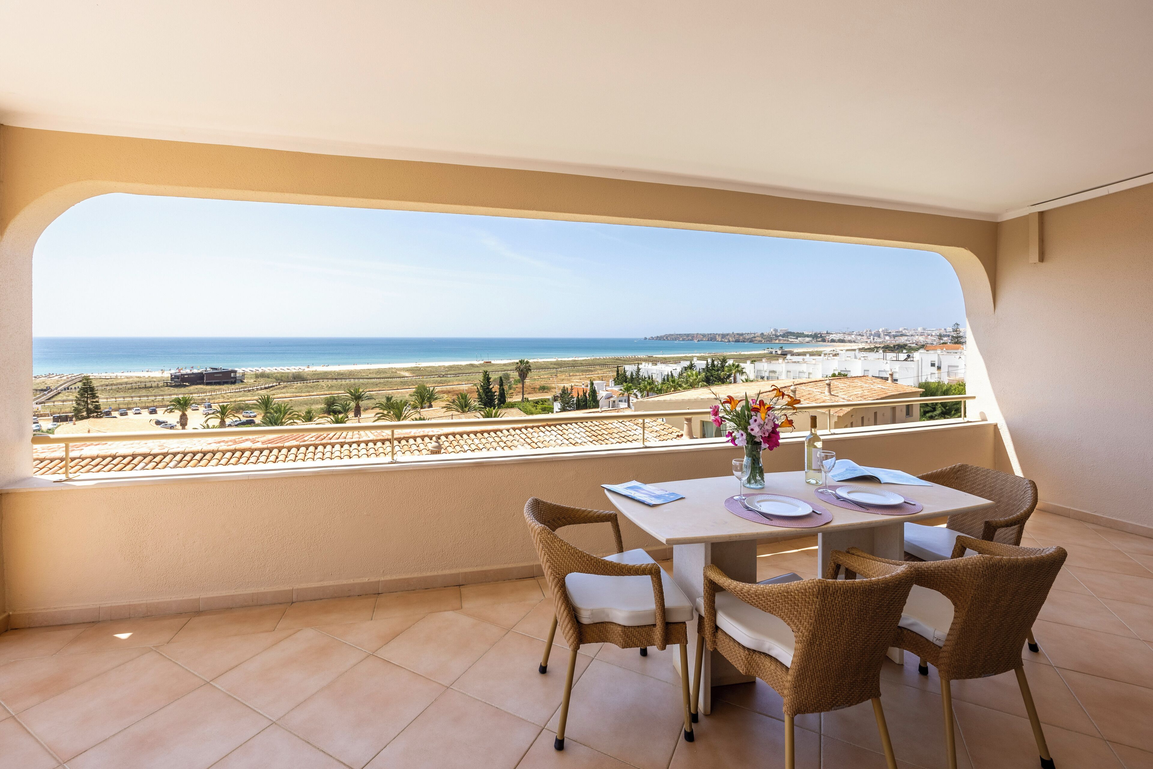 A balcony with a table set for two, overlooking a coastal landscape.