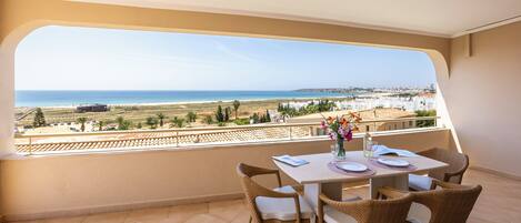 A balcony with a table set for two, overlooking a coastal landscape.