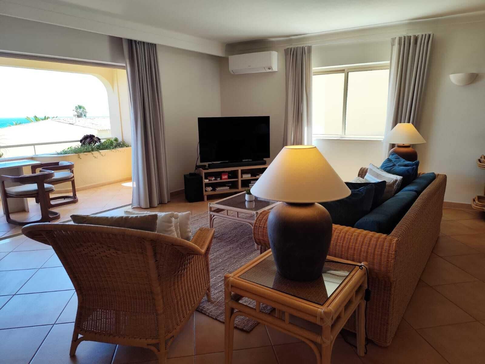 A living room with a television, wicker furniture, a lamp, and a view of the sea.