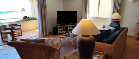 A living room with a television, wicker furniture, a lamp, and a view of the sea.