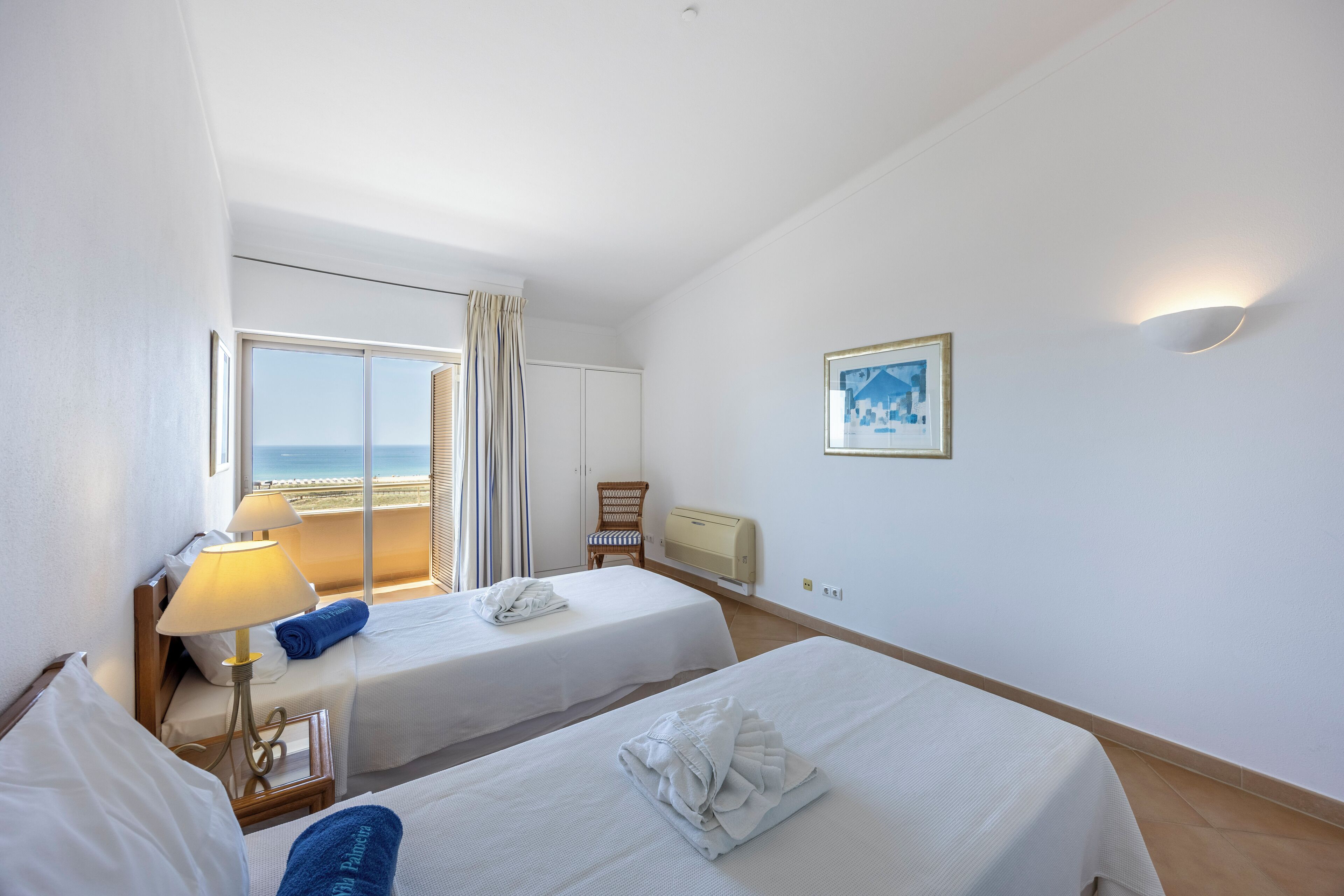 Une chambre d’hôtel avec deux lits, une fenêtre avec des rideaux, une lampe, une chaise et un climatiseur fixé au mur.