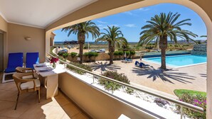 Un balcone con vista su una piscina, palme e una città in lontananza.