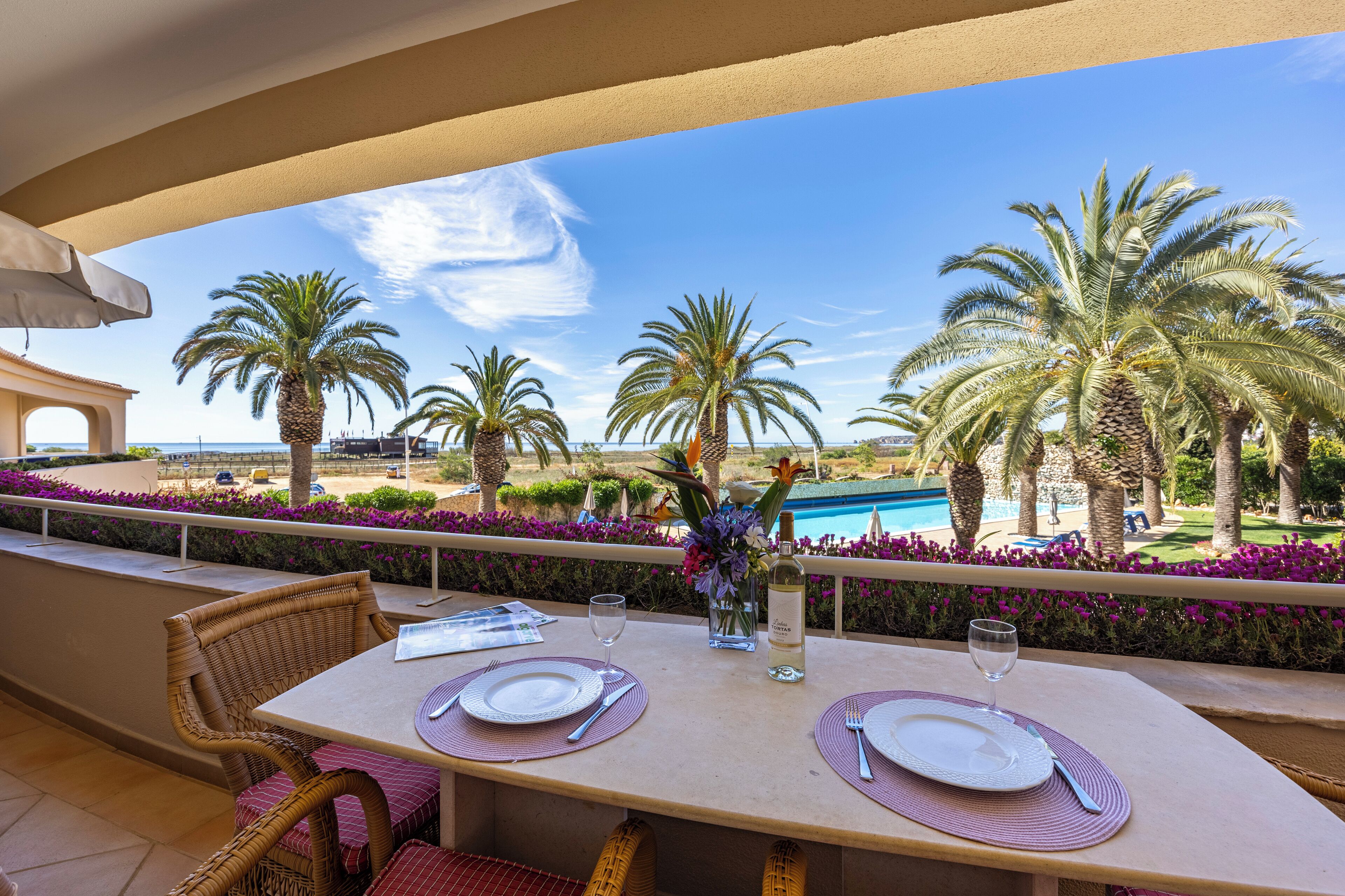 A dining area with two tables set for two, overlooking a pool and palm trees.