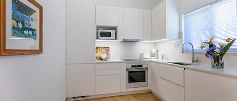 A modern kitchen with white cabinets, a microwave, an oven, and a sink.