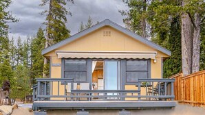 Une petite cabane à un seul étage, dotée d’une véranda, d’une cuisine visible et d’une terrasse.