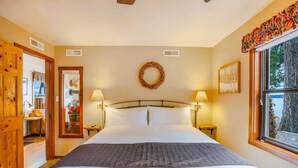 Une chambre à coucher avec un lit, deux lampes de chevet, une fenêtre donnant sur un paysage agréable, une porte menant à une autre pièce et une guirlande décorative accrochée au mur.