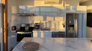 Una cocina moderna con armarios blancos, un refrigerador de acero inoxidable, una cafetera y un hervidor.