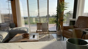 Una sala de estar moderna con un ventanal grande, un sofá, un sillón, una mesa de centro y una planta en maceta.