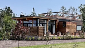 Una casa moderna de dos pisos con fachada de madera, ventanas amplias y un balcón.