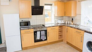 Una cocina compacta con armarios de madera, horno empotrado, microondas, tostadora y lavadora.
