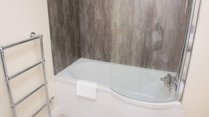 Un baño moderno con bañera de hidromasaje con cerramiento de vidrio, toallero cromado y pared con textura de madera.