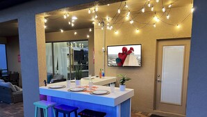 An outdoor bar area with a counter, stools, and string lights. - Themed 8BR: Game Room • 2 Theaters • Pool & Spa (Kissimmee)