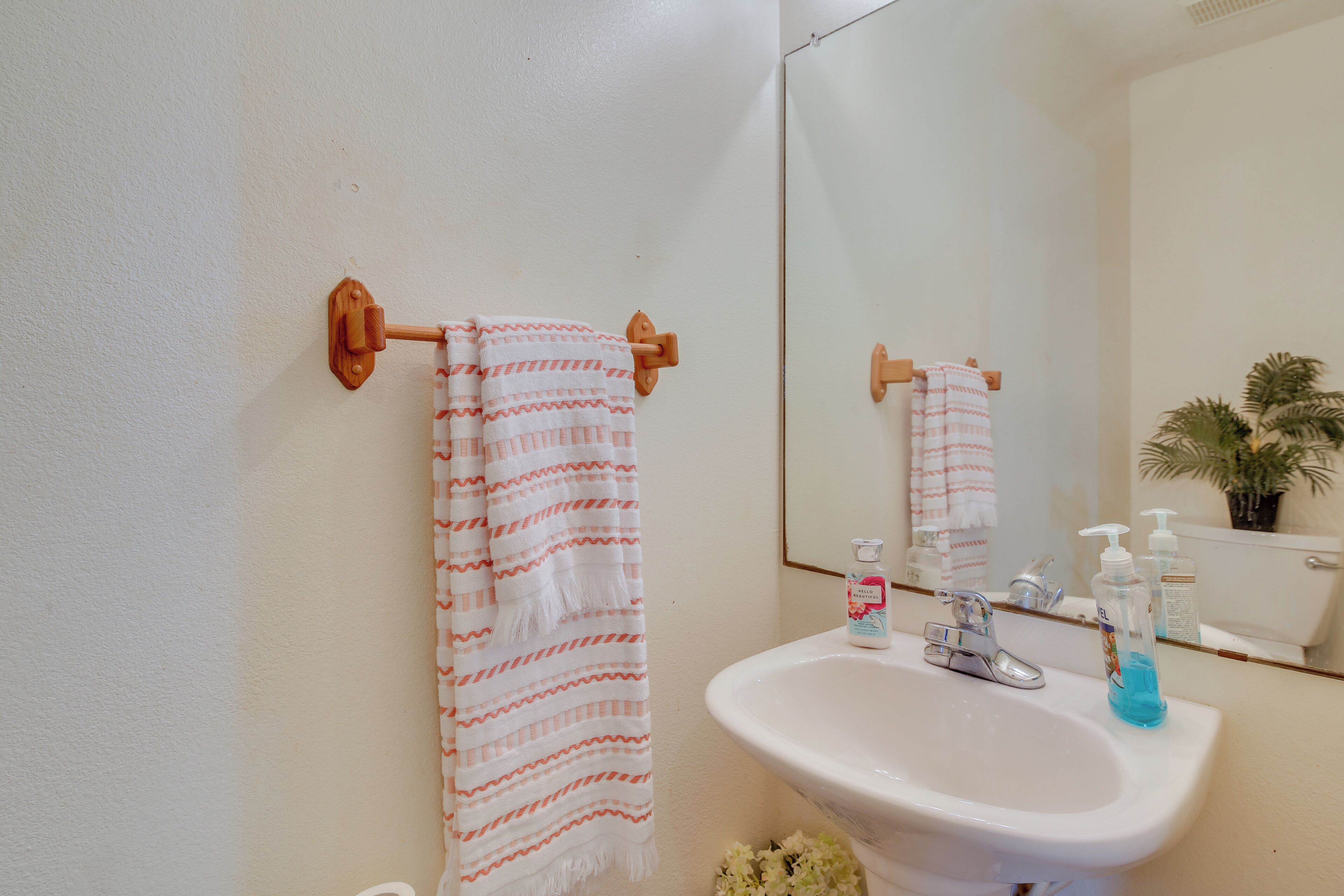 Une salle de bain avec un lavabo blanc, deux flacons de savon pour les mains et une serviette suspendue à un porte-serviettes en bois.