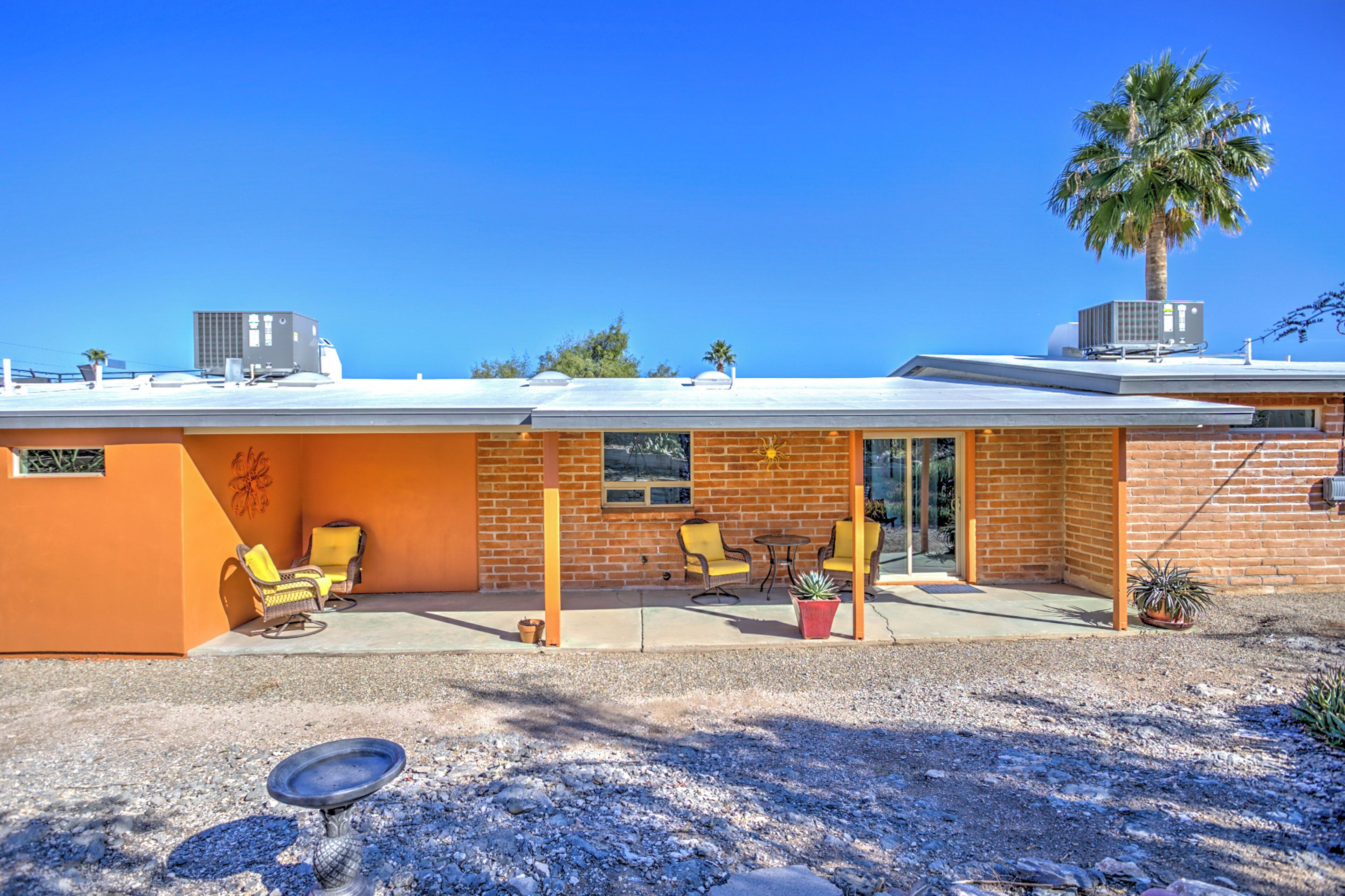 A modern building with a brick facade, outdoor seating area, and a palm tree.