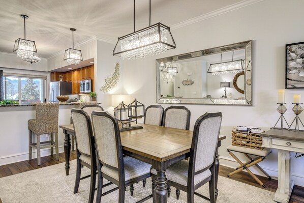 A dining area with a wooden table, upholstered chairs, and hanging crystal chandeliers.