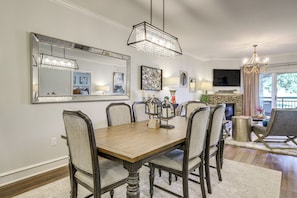 A dining area with a wooden table, six chairs, a chandelier, a large mirror, and a television in the background.