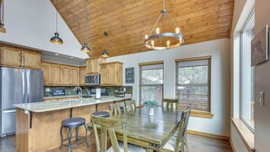 A kitchen with wooden cabinets, a stainless steel refrigerator, a large island with stools, and pendant lighting. - Angel Fire Cabin w/ Deck: 3 Mi to Ski Lifts! (Angel Fire)