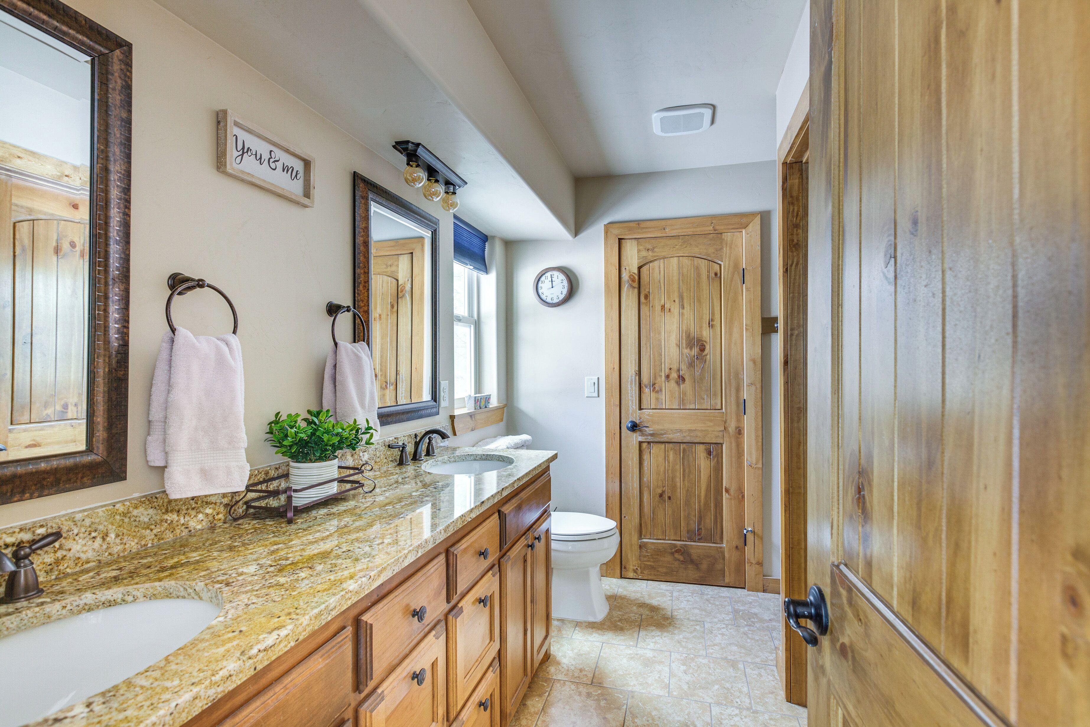 A bathroom with a wooden door, a sink, a mirror, and a clock on the wall.