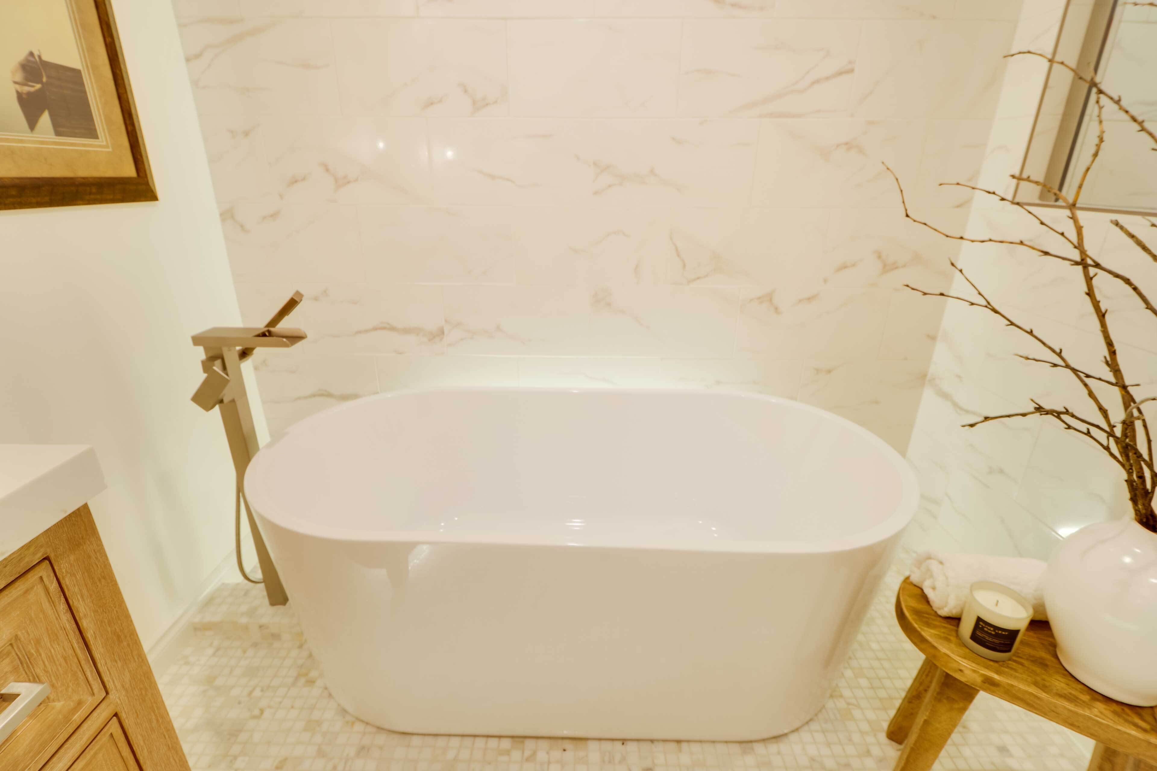 A modern bathroom with a freestanding bathtub, marble walls, and a wooden vanity.