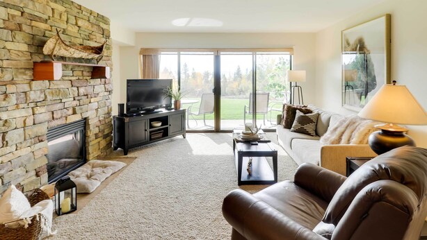 A living room with a stone fireplace, a television, a sofa, and a view of the outdoors through a sliding glass door.