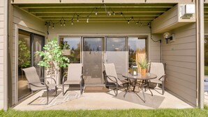A covered patio with a table and chairs, a potted plant, and a string of lights.