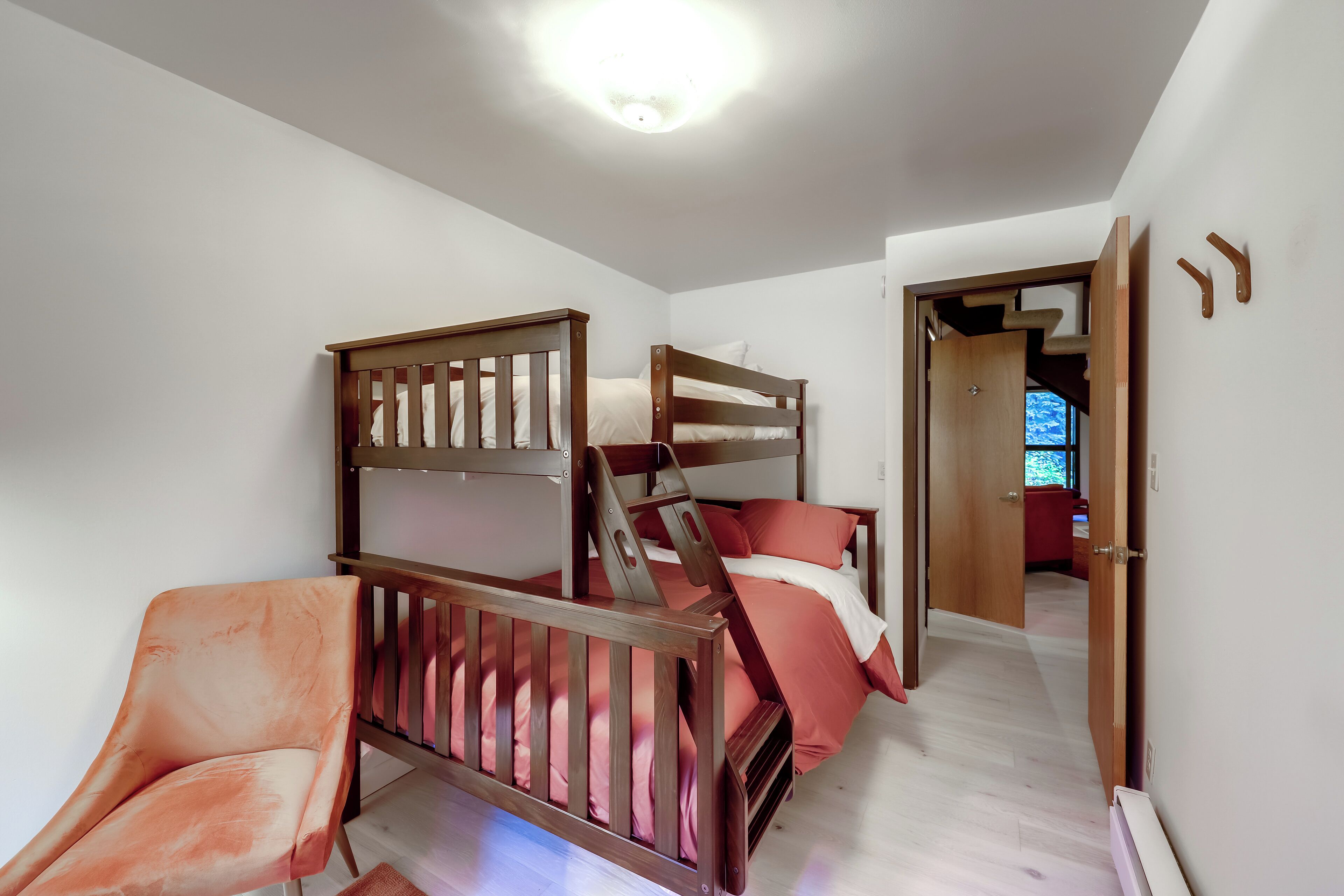 A bedroom with a bunk bed, a chair, and a door leading to another room.