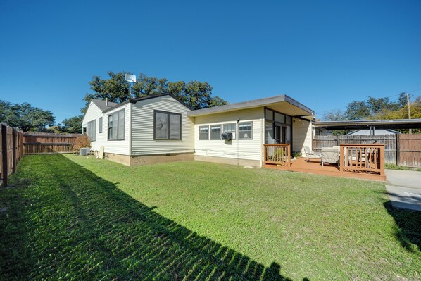 A single-story mobile home with a fenced backyard, a patio with outdoor furniture, and a clear blue sky.