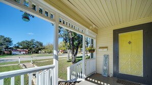 Un porche avec une porte jaune, des balustrades blanches et une pancarte indiquant « Bienvenue ».