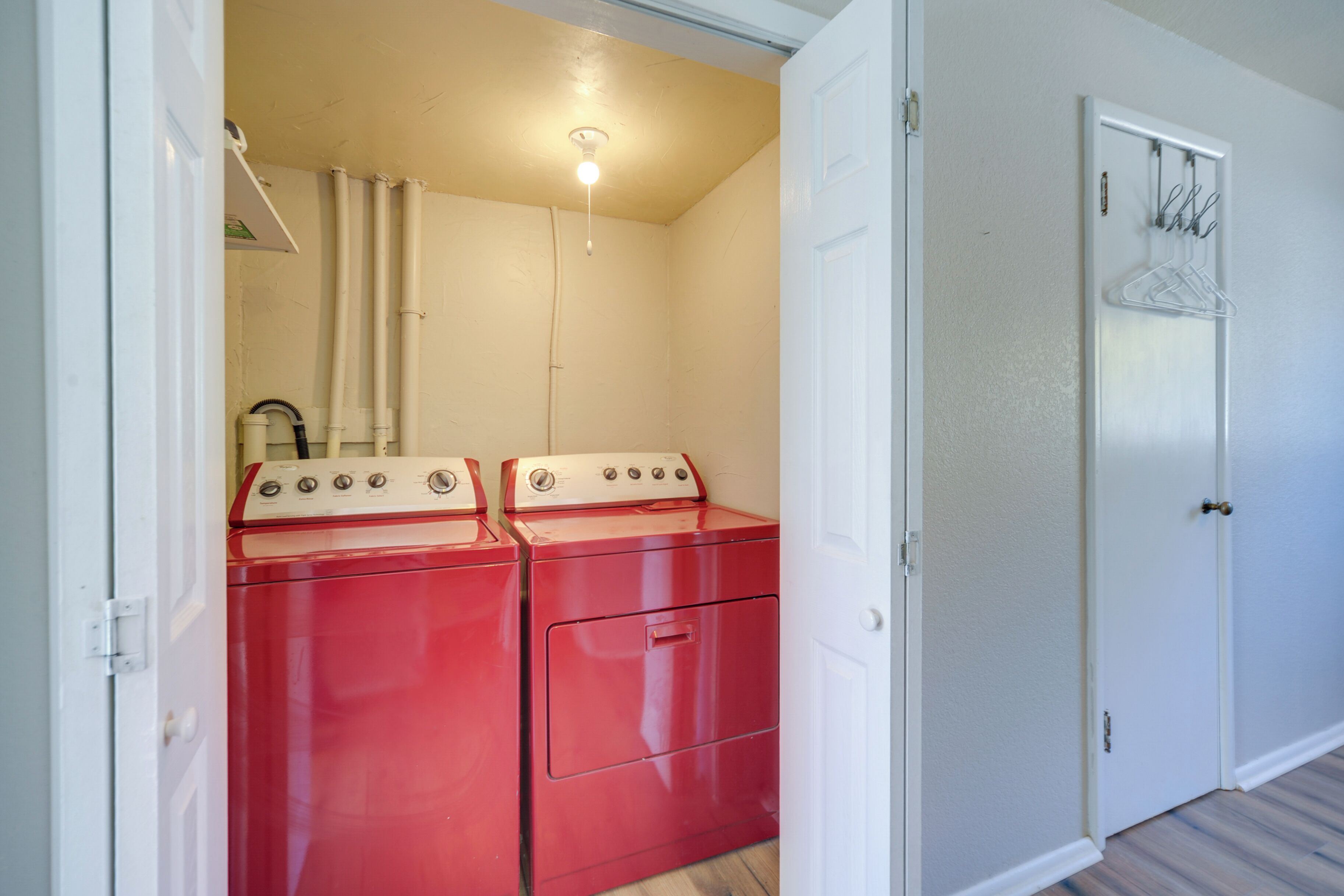 A compact room with a red washer and dryer, a white door, and a coat rack.