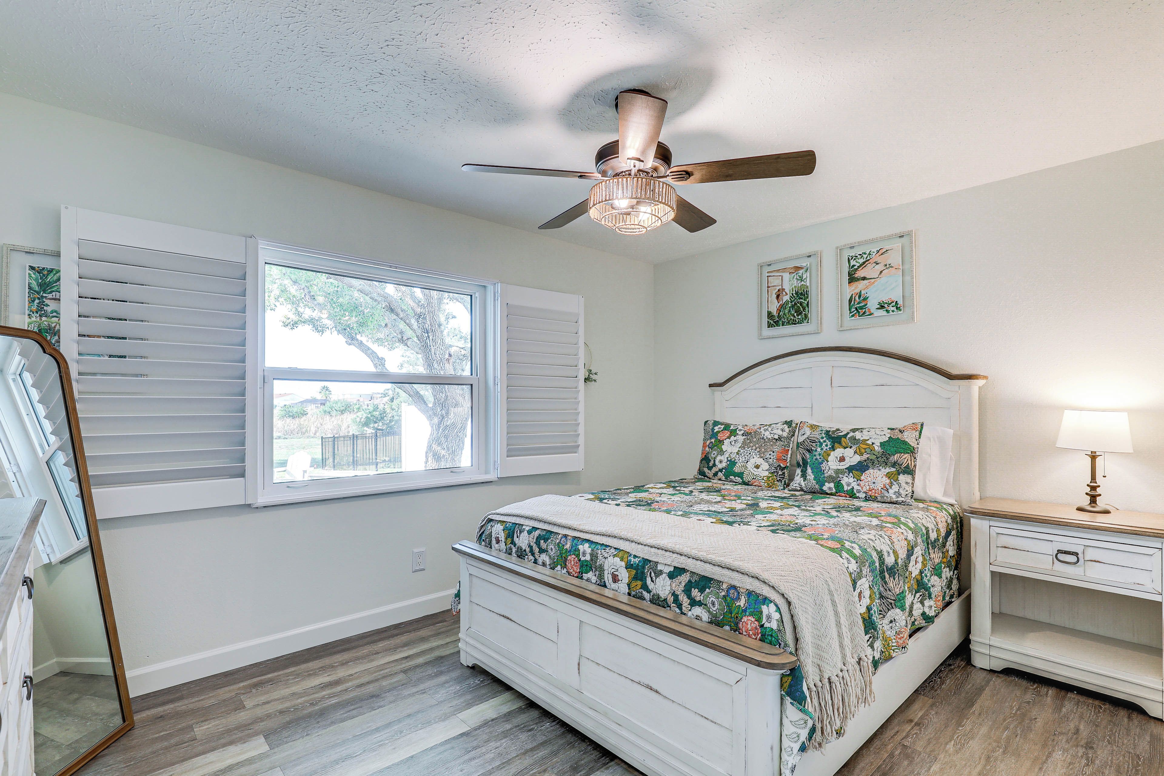 A bedroom with a bed, a nightstand, a ceiling fan, and a window with shutters.