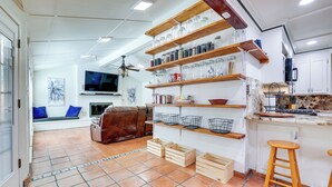 Une cuisine avec des étagères en bois, un téléviseur et un coin salon comprenant un canapé et des coussins.