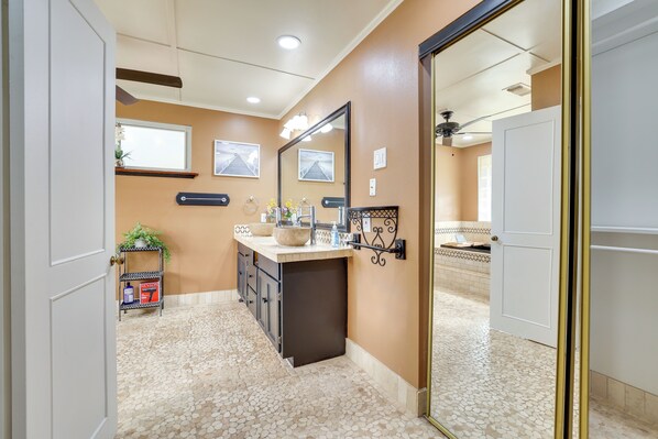 A bathroom with a vanity, a mirror, a shelf with toiletries, and a tiled floor.