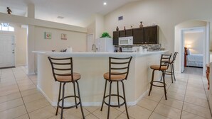 A kitchen with a central island, bar stools, a microwave, cabinets, and a refrigerator. - Pet-friendly Port St Lucie Home ~ 5 Mi to Marina! (Port Saint Lucie)