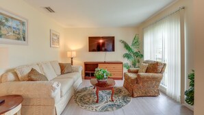 A living room with a sofa, armchair, coffee table, TV, and a large window with curtains. - Pet-friendly Port St Lucie Home ~ 5 Mi to Marina! (Port Saint Lucie)