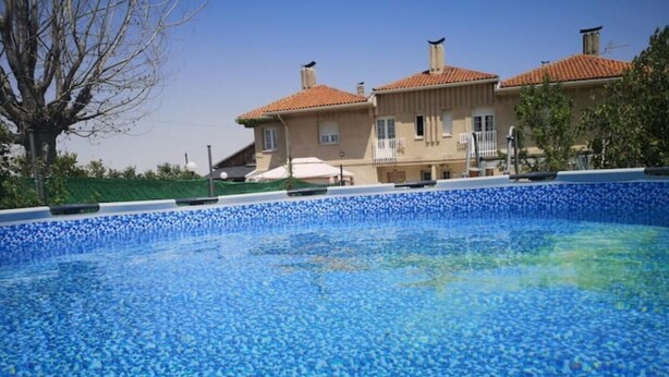 Ein Schwimmbecken mit blau mosaikbesetztem Rand, umgeben von einem Gebäude mit einem gefliesen Dach und Balkonen.