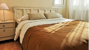 Ein Schlafzimmer mit einem Holzkopfende, einem Nachttisch mit Schubladen, einer Lampe und einem Fenster mit Vorhängen.