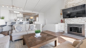 A modern living room with a fireplace, a sofa set, a coffee table, and a kitchen in the background. - Cardiff Panoramic Paradise - Stunning Ocean Views (Cardiff By The Sea)
