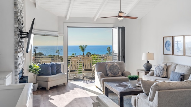 A spacious living room with a view of the ocean, a ceiling fan, and a comfortable seating area. - Cardiff Panoramic Paradise - Stunning Ocean Views (Cardiff By The Sea)