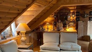 A cozy attic room with a sloped ceiling, a sofa, a chair, and a table with decorative items. - Appartement D'exception Type Chalet Avec vue sur les Toits Saint Honoré / Louvre (Paris)
