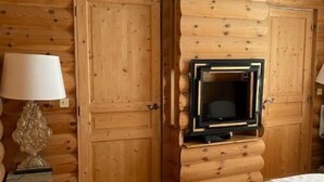 A wooden room with a bed, a TV mounted on the wall, and a lamp on a small table. - Appartement D'exception Type Chalet Avec vue sur les Toits Saint Honoré / Louvre (Paris)