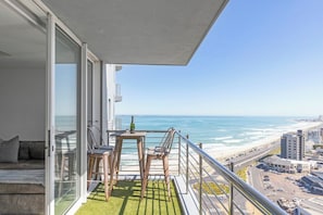 Ein Balkon mit Blick auf das Meer, ein Tisch mit Stühlen und eine Couch.
