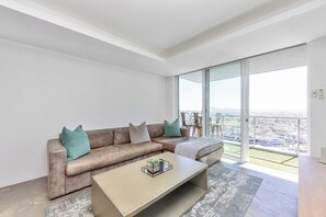 A modern living room with a sectional sofa, a coffee table, and a large sliding glass door leading to a balcony with a city view.