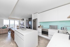 A modern kitchen with white cabinetry, a central island, and a view to the outside. - Sea View Apartment with pool, Blouberg, Sleeps 4 (Cape Town)