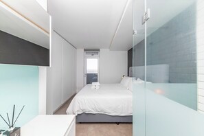 Ein modernes Hotelzimmer mit Bett, einer Glastrennwand und Blick auf die Stadt.