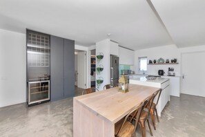 Cozinha moderna com ilha central, área de jantar com mesa e cadeiras de madeira, e vista para a sala de estar adjacente.