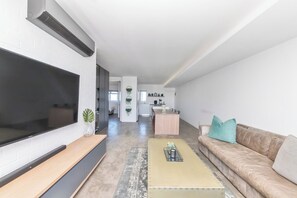 A modern living room with a large flat-screen TV, a beige sofa, and a coffee table.